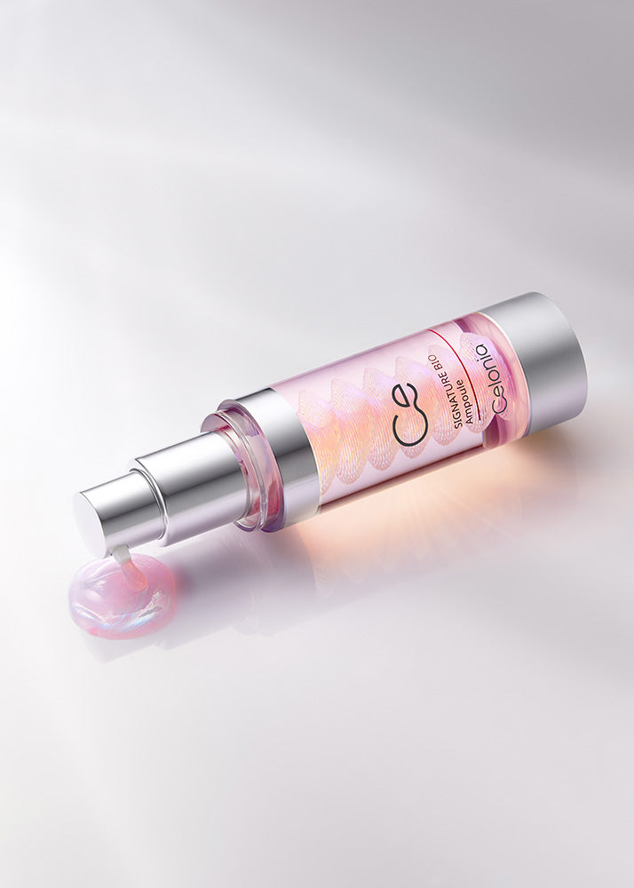 Cosmetic serum bottle with pink cap and visible brand logo on a light gray background
