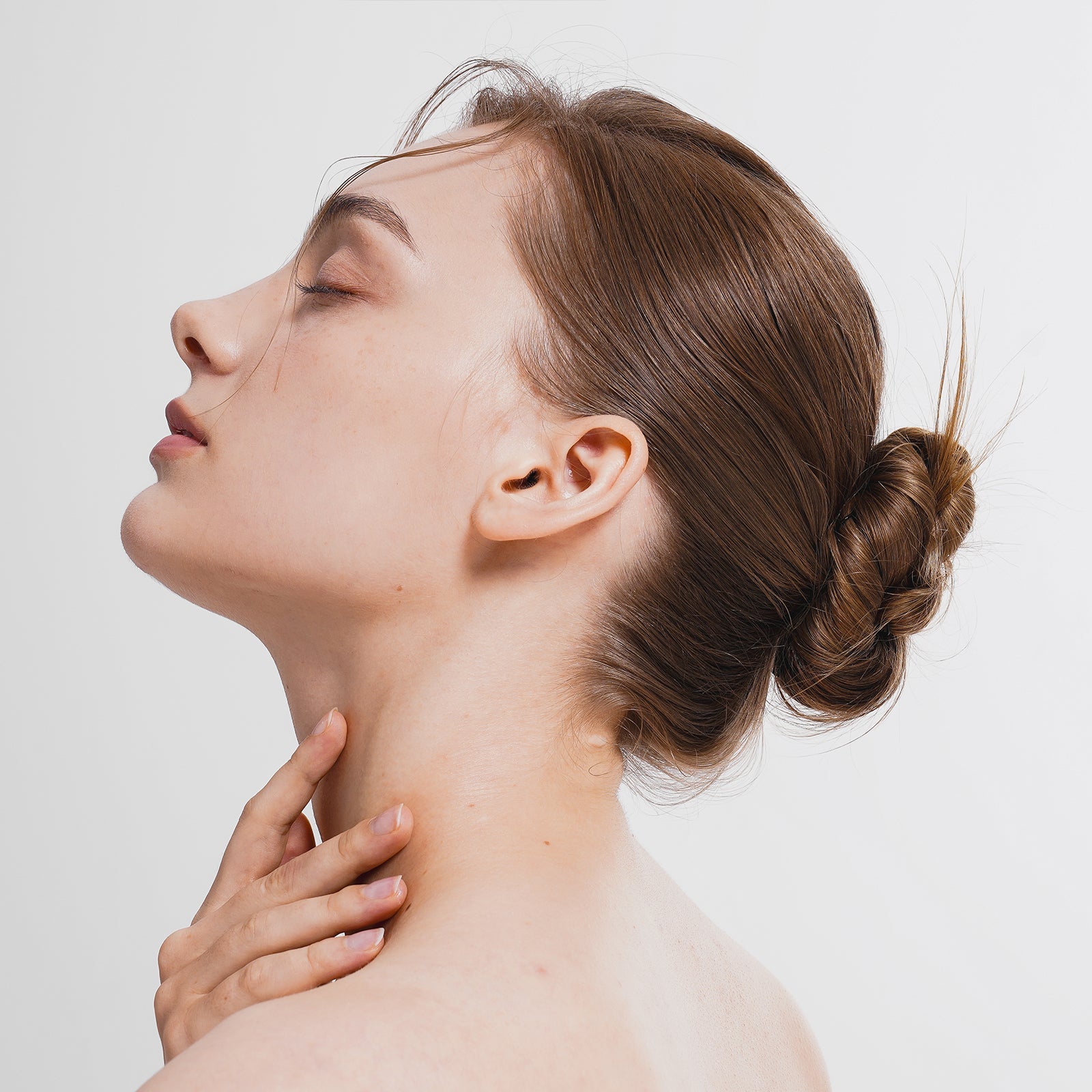 Profile of a woman with glowing skin and elegant bun hairstyle gently touching her neck, showcasing natural beauty