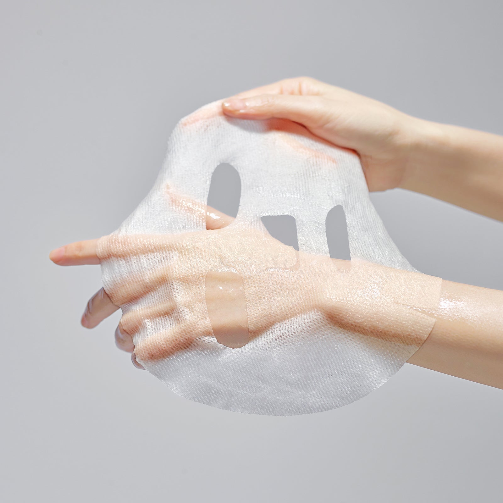 Hands holding a hydrating sheet mask for facial skincare, showing soft and translucent texture before application